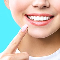 Nose to neck view of woman pointing to her bright white smile