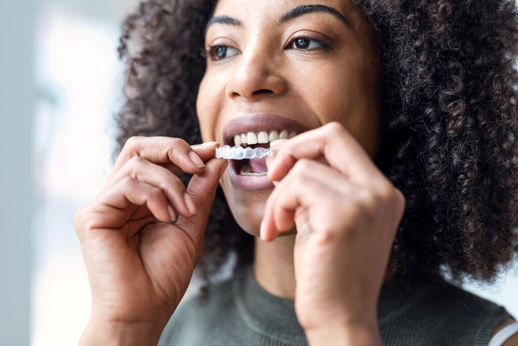 Woman with dark curly hair placing Invisalign over upper arch